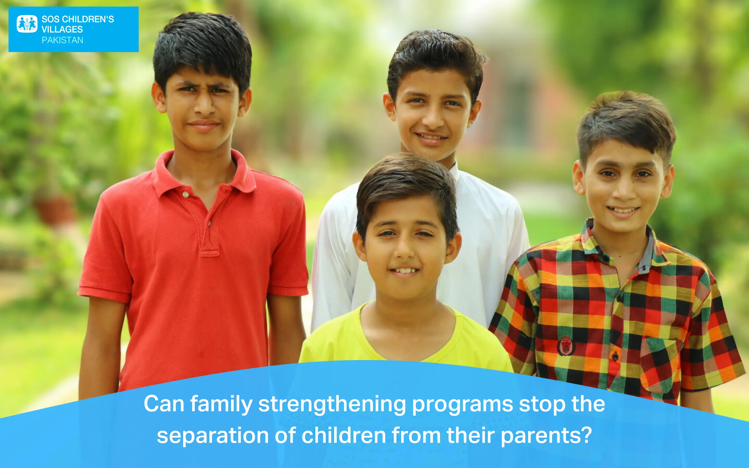 Four smiling boys standing together outdoors with a blurred green garden background.